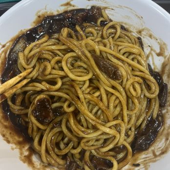 Young Chow Loo - Jjajang Noodle mixed - A white plate contains stir-fried noodles with dark sauce and sliced mushrooms, with some sauce spilled on the plate's edges. - Korean Near Me - Burlington, Massachusetts