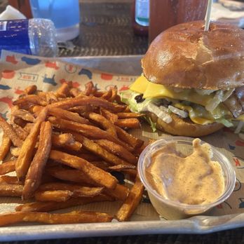 Kelsey's - Bacon bourbon burger - A burger with cheese, lettuce, and bacon on a bun, served with a side of fries and a dipping sauce on a tray. - American Near Me - Niagara Falls, Ontario