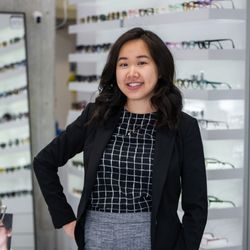 Specs & Spines Optometry and Chiropractic - Dr. Christine Ly standing in front of a wall of eyeglasses inside Specs & Spines Optometry in Toronto.