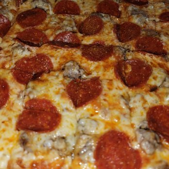 Pizza House - Close-up - The image depicts a close-up view of a pizza topped with pepperoni slices, melted cheese, and mushrooms. The crust is thin and crispy, with the toppings evenly distributed across the surface. The cheese appears melted and slightly browned in some areas, with the pepperoni slices showing a cooked, slightly curled appearance. The focus is on the pizza's surface, highlighting the texture of the toppings and cheese. - Pizza Near Me - Springfield, Missouri