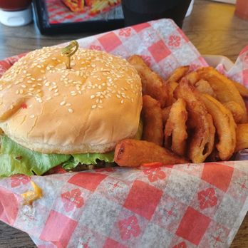 Laguna Burger - Laguna Burger with onion petals - A cheeseburger with a sesame seed bun, lettuce, and a toothpick is placed on checkered paper. It is accompanied by fried onion rings and potato fries, served on a basket at a casual dining restaurant. - Burgers Near Me - Albuquerque, New Mexico