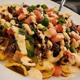 Brisket Frito Pie - A plate of brisket frito pie features tortilla chips topped with shredded brisket, chopped tomatoes, and sliced green onions. The dish is drizzled with a creamy sauce and served on a white plate. The image includes a timestamp of March 09, 2024, 4:51 PM, indicating when the photo was taken.