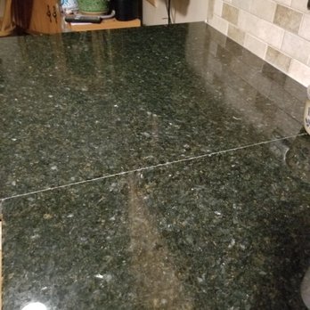 Rock Solid Tops - After install, seam not color matched.  Requested they come back. Did not show for 1st appt. - A polished dark green granite countertop with a visible seam runs across the kitchen, showing water spots and reflections. - Countertop Installation Near Me