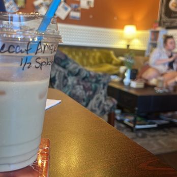 Lucille's Cafe - A glass of iced drink with a blue straw is placed on a wooden table in a cafe setting, with a blurred background of seating and decor. - Cafes Near Me - Ledyard, Connecticut