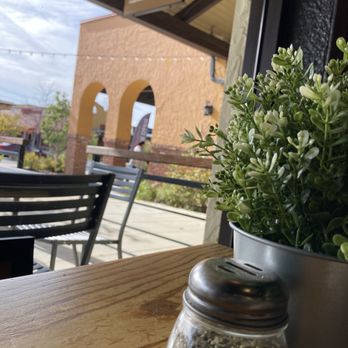 Pizza Stop - Nice atmotsphere. - Inside a restaurant or cafe, a wooden table holds a potted plant and a spice jar, with outdoor seating and a building with arches visible outside. - Pizza Near Me - Silver Spring, Maryland
