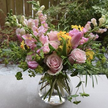 Fleurelity - A bouquet of pink roses, yellow and pink lilies, and other mixed flowers in a clear glass vase on a white table outdoors. - Florists Near Me - Oakton, Virginia