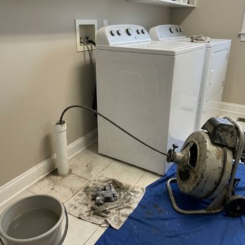 Always Clear Sewer and Drain - A laundry room features washing machines, a portable drain cleaning machine, hoses, a bucket, and cleaning cloths, illustrati... - Plumbing Near Me Always Clear Sewer and Drain - A laundry room features washing machines, a portable drain cleaning machine, hoses, a bucket, and cleaning cloths, illustrati... - Plumbing Near Me