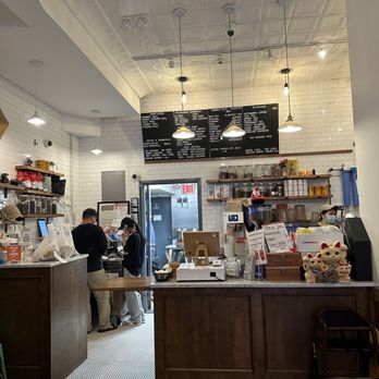 Hanco’s - Inside - A cafe interior with a white tiled wall, a black menu board, and staff at the counter. The ceiling has decorative molding and hanging lights. - Vietnamese Near Me - Brooklyn, New York