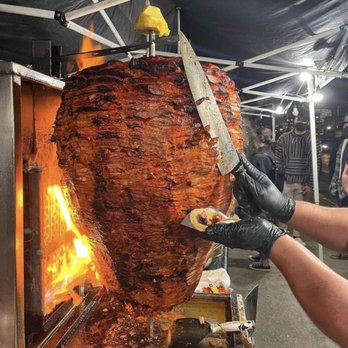 Tacos El Venado - a man holding a knife over a large meat - Food Trucks Near Me - Los Angeles, California Tacos El Venado - a man holding a knife over a large meat - Food Trucks Near Me - Los Angeles, California