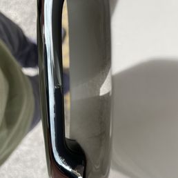 The handle on the driver side door also peeling off as a result of whatever product they used to wash my car. - Close-up of a car door handle showing peeling paint and surface damage, with part of the car's body visible.