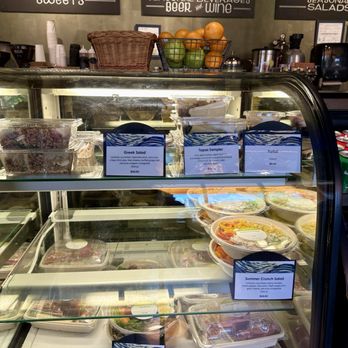 Van Gogh Cafe - A glass refrigerated display case contains pre-packaged salads and food items, with labels indicating different salad options like Greek Salad and Tuna Nicoise Salad. - Cafes Near Me - Hamilton, New Jersey