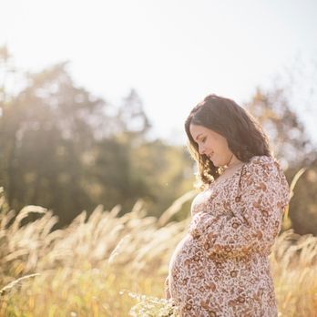 Ashlee Wilcox Photography - Maternity photo. Expectant mother to be stands in a golden field of grass, holding wildflowers and smiling down at her baby bump. - Session Photography Near Me Ashlee Wilcox Photography - Maternity photo. Expectant mother to be stands in a golden field of grass, holding wildflowers and smiling down at her baby bump. - Session Photography Near Me