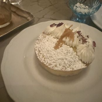 Sofreh - A round dessert topped with whipped cream, powdered sugar, and caramel, served on a white plate in a restaurant setting. - Persian/Iranian Near Me - Brooklyn, New York