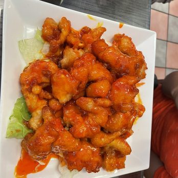 Thai Station - Outstanding orange chicken! Enormous portion! - A square white plate holds orange chicken coated in a glossy sauce, with some lettuce underneath, on a dark table. - Thai Near Me - Payson, Arizona