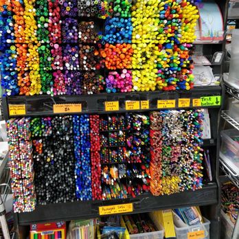 Austin Creative Reuse - Pencils, pens, and markers bundles for 25 cents - The image shows a multi-tiered black shelving unit filled with a wide variety of markers, pens, and craft supplies. The top shelf contains bundles of markers and highlighters, with handwritten signs indicating prices and categories such as 'Paint Markers 5¢' and 'Highlighters 10¢'. The middle shelf displays more markers and pens, organized in sections with labels like 'Stick/Basic Pens 5¢' and 'Twist Crayons 5¢'. The bottom shelf has plastic containers labeled for different supplies, including markers, pens, and pencils, with some items in packaging. The setup appears to be in a community reuse center, promoting affordable art and craft materials. - Fabric Stores Near Me - Austin, Texas