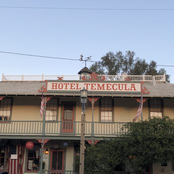 Old Town Temecula - Hotel Temecula. - The image shows the front of Hotel Temecula, a historic building with a sign on the roof, a balcony, and American flags. - Local Flavor Near Me - Temecula, California