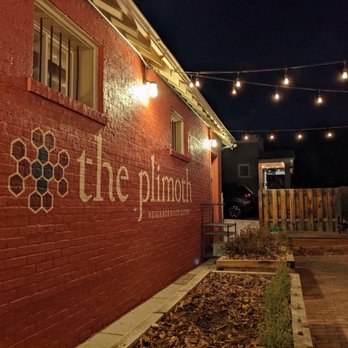 The Plimoth - Nighttime view of The Plimoth restaurant's brick exterior wall with signage, string lights overhead, and a small outdoor area. - Italian Near Me - Denver, Colorado