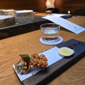 Koju - The Asparagus!!!! Wow! - A Japanese appetizer featuring a fried roll with a green garnish, lemon wedge, and small dollops of sauce on a black rectangular plate. - Japanese Near Me - Brooklyn, New York