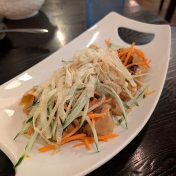 Dumpling Cafe - Spicy pork dumplings topped in a veggie slaw - A dish featuring dumplings topped with shredded cucumber, carrots, and crispy strips, served on a white plate at a restaurant. - Dim Sum Near Me - Santa Fe, New Mexico