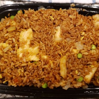 China Cafe - Fried Rice - A black plastic container holds fried rice mixed with peas, scrambled eggs, and small vegetable pieces. The rice appears well-cooked and seasoned, with visible bits of egg and green peas distributed throughout. The dish is placed on a speckled countertop, and part of a cloth or paper towel is visible at the top of the image. - Chinese Near Me - Chantilly, Virginia