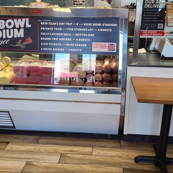 Jersey Mike's Subs - A refrigerated display case contains wrapped food items, with a sign above advertising a stadium experience package. - Fast Food Near Me - Bloomington, Indiana