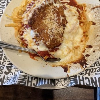 Pahgre's - Chicken Parmesan al Forno - A plate contains chicken parmesan topped with melted cheese and grated cheese, served over pasta with tomato sauce. The dish is garnished with a breaded chicken cutlet and appears to be in a restaurant setting, with a spoon on the plate and a patterned table surface. - Pizza Near Me - Montrose, Colorado