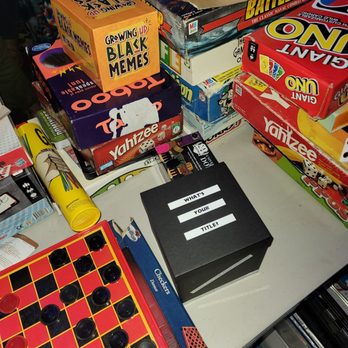 The Mixx Pasadena - Game night - The image shows a table with multiple board games, including chess, checkers, and other boxed games, along with a black box labeled 'WHAT'S YOUR TITLE?' and a small orange box labeled 'Growing Up Black Memes.' - New American Near Me - Pasadena, California