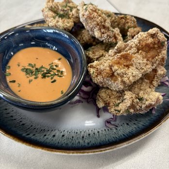 Azure - A ceramic plate holds several pieces of fried chicken with a golden-brown, crispy coating. A small blue bowl contains an orange-colored dipping sauce garnished with chopped herbs. The plate is placed on a light-colored table surface, with a blurred background. - Desserts Near Me - Austin, Texas