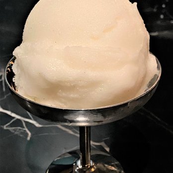 Geppetto - A single scoop of pale, creamy sorbet is placed in a shiny metal dish with a stem, set on a dark surface. The sorbet appears smooth and well-formed, with a slightly rounded top. The background is dark and out of focus, emphasizing the dessert as the main subject. - Italian Near Me - Cambridge, Massachusetts
