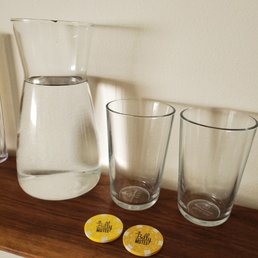 a pitcher, glasses, and coasters on a shelf a pitcher, glasses, and coasters on a shelf