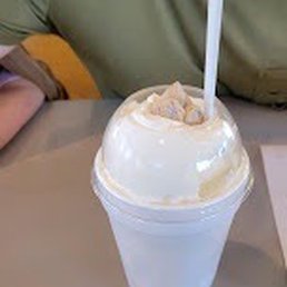 a woman sitting at a table with a cup of ice cream a woman sitting at a table with a cup of ice cream