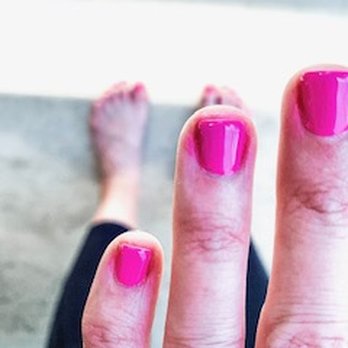 Yogani Nails And Spa - A close-up of fingers showing bright pink nail polish, with a blurred background of feet and a floor. - Waxing Near Me - Ormond Beach, Florida