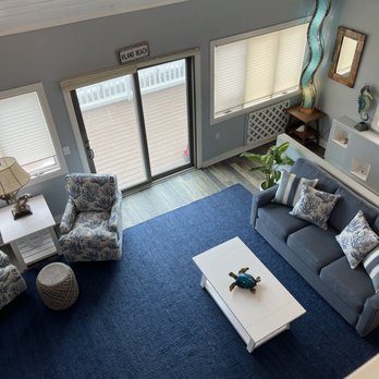 Everything Cool  - A living room features a blue carpet, a gray sofa with patterned pillows, an armchair with a coastal pattern, and decorative items including a turtle figurine on the coffee table. - Furniture Stores Near Me - St Augustine , Florida