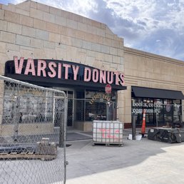 Outside with construction, but still open! - Exterior view of Varsity Donuts in Manhattan, KS, showing the storefront with construction fencing, equipment, and signage, indicating ongoing renovations.