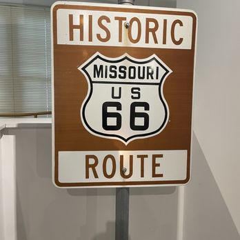 Route 66 State Park - Historic Route 66 sign - A rectangular sign with a brown and white background shows the words "HISTORIC" at the top and "ROUTE" at the bottom. The center features the U.S. Route 66 shield, with "MISSOURI" written inside the top portion of the shield. The sign is mounted on a metal pole and appears to be an indoor display, with a background of a white wall and ceiling grid. - Parks Near Me - Eureka, Missouri