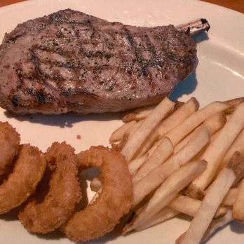 Black Angus Steakhouse - Bone-in ribeye (served rare, as requested) with onion rings and fries. - Steakhouses Near Me - Montclair, California
