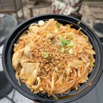 Thai Table & Kitchen - Chicken pad Thai - A takeout bowl of chicken pad Thai featuring rice noodles, cooked chicken pieces, chopped green onions, and crushed peanuts, set outdoors. - Thai Near Me - Pittsburgh, Pennsylvania