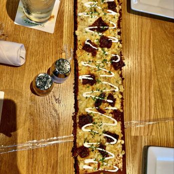 Seasons 52 - Flatbread - A rectangular flatbread with cheese, meat toppings, chopped herbs, and white sauce drizzle, served on a wooden table. - New American Near Me - Albuquerque, New Mexico