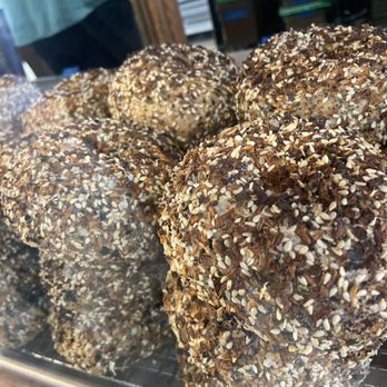 Sunday Bagels - Everything Bagels! - Several bagels covered with sesame seeds and other toppings are displayed on a wire rack at a market stall. - Bagels Near Me - Albuquerque, New Mexico