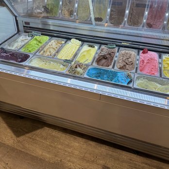 Stop N Dip - A glass display case shows multiple gelato flavors, including green, yellow, pink, and brown, with some labeled and garnished. - Desserts Near Me - Elgin, Illinois