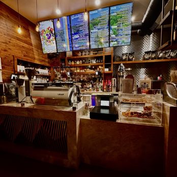 The Coffee Builders - Front counter and Menu - A coffee shop counter with digital menu screens, coffee brewing equipment, and a display case of baked goods, set against wooden and metallic decor. - Coffee & Tea Near Me - Phoenix, Arizona