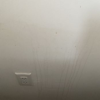 Sandia Green Clean - Bedroom wall behind bed still covered in filth. - A plain white wall with dirt marks and streaks, featuring an electrical outlet near the bottom left corner. - Home Cleaning Near Me - Albuquerque, New Mexico