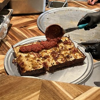 AJ's Pizza Joint - Pouring sauce on a Detroit pizza - Pizza Near Me - Winter Garden, Florida AJ's Pizza Joint - Pouring sauce on a Detroit pizza - Pizza Near Me - Winter Garden, Florida