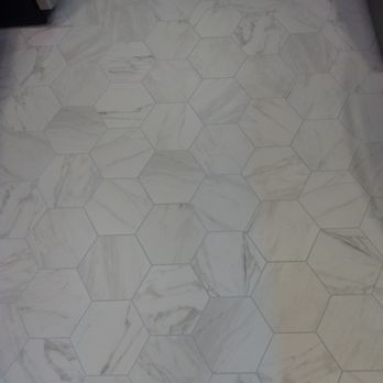 Junior Tile installation - Kitchen after - The image shows a floor covered with white marble tiles arranged in a hexagonal pattern. Each tile features natural gray veining, adding texture and visual interest. The tiles are fitted closely together with visible grout lines, and the setting appears to be indoors, possibly in a kitchen or bathroom area. - Tiling Near Me