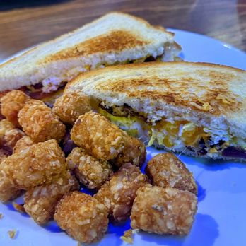 Effingbar And Grill - Brunch Special - A white plate holds a grilled sandwich cut in half, revealing melted cheese and meat filling. Next to the sandwich are several fried chicken bites and a strip of bacon. The food is served on a wooden table, suggesting a casual dining setting. - American Near Me - Albuquerque, New Mexico