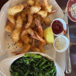 Fried Shrimp - A plate of fried shrimp with breading, served with lemon, ketchup, and tartar sauce, alongside sautéed greens, on a white dish.