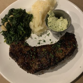 Flatiron - Incredible New York strip, mashed potatoes and spinach. - A dinner plate featuring a grilled steak with herbs, mashed potatoes, sautéed greens with pine nuts, and a side of herb butter. - Steakhouses Near Me - Red Hook, New York
