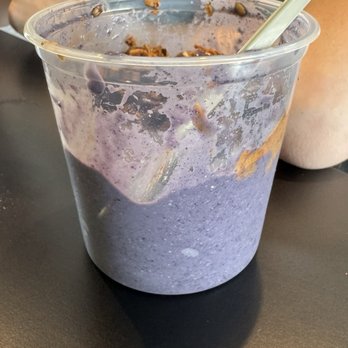BeneBlends - Blueberry Pie Bowl (LG) - A clear plastic container with remnants of a purple smoothie bowl, a spoon, and a straw, placed on a black table in a casual setting. - Juice Bars & Smoothies Near Me - Madison, Wisconsin