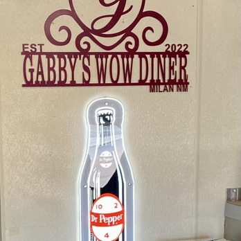 Gabby's Diner - Logo - A neon-lit Dr. Pepper bottle is mounted on a wall, with a logo for Gabby's Wow Diner in Milan, NM, displayed above it. - American Near Me - Milan, New Mexico