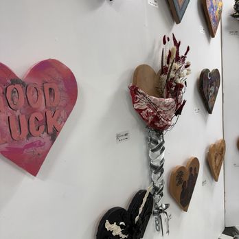The Mosaic Workshop - Multiple heart-shaped artworks and a floral arrangement are mounted on a white gallery wall, with small labels indicating details. - Art Classes Near Me - Austin, Texas